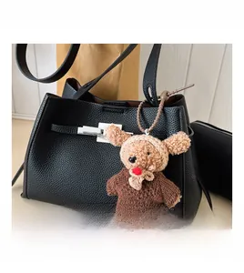 Detail of black litchi leather handbag with silver lock and brown knitted bear charm