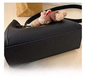 Close-up of black pebble leather texture and a cute knitted teddy bear charm on the bag