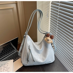 Detail of grey leather tote bag with silver zipper and cute teddy bear charm accessory
