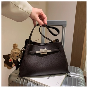 Detail of dark brown lychee leather handbag with silver clasp and cute plush bear charm