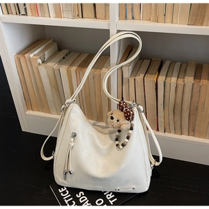 Detail of creamy white large hobo bag with teddy bear charm against a bookshelf
