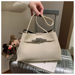 Close-up of beige lychee grain leather bag with silver metal clasp and a bear pendant