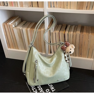 Detail of light green hobo bag with side zipper and cute plush bear charm on a bookshelf