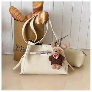 Close-up of beige lychee grain leather shoulder bag with silver clasp and bear charm