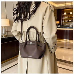 Modèle portant un sac seau en cuir marron foncé avec un manteau beige dans un intérieur chic