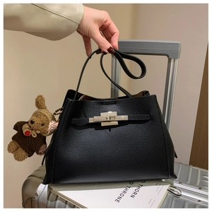 Detail of black lychee leather handbag with silver metal lock and cute bear charm pendant
