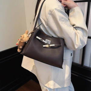 Detail view of dark brown pebbled leather shoulder bag with silver lock and bear charm