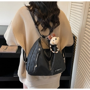 Detail of black pebbled leather tote showing the functional zipper and plush bear charm