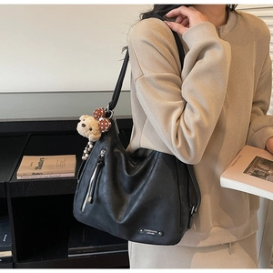 Detail of black PU leather tote bag with vertical zipper and cute plush bear charm