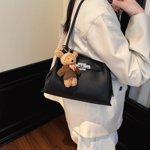 Detail of black lychee leather handbag with silver lock and a brown plush bear charm