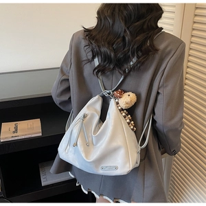Detailed back view of a white crescent tote bag with cute bear charm on a female model