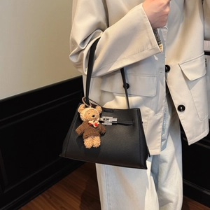 Detail of black litchi leather handbag with silver rotary lock and cute bear charm