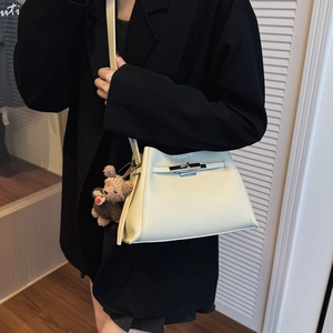 Detail shot of beige pebble grain handbag with silver clasp and bear charm on model