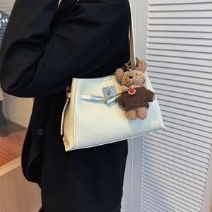 Close-up of beige lychee grain leather bag with silver metal lock and cute bear charm