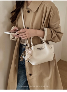 Schicke cremefarbene Leder-Eimertasche mit silbernem Schloss und Alpaka-Anhänger am Trenchcoat