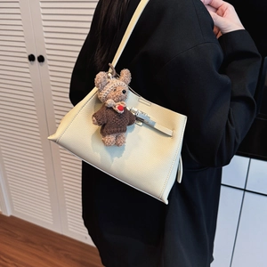 Detail of beige lychee leather bag with silver twist lock and cute teddy bear charm