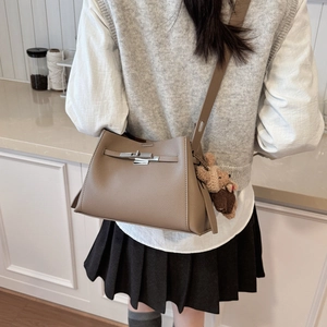 Detail view of brown pebbled leather crossbody bag with metal twist lock and bear charm