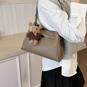Detailed view of taupe lychee leather trapezoid handbag with silver buckle and bear charm