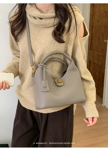 Detail der grauen Beuteltasche aus Leder mit Goldverschluss und Markenanhänger am Modell