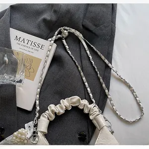 Detail der cremeweißen Handtasche mit Faltenhenkel und silberner Kette auf grauem Blazer
