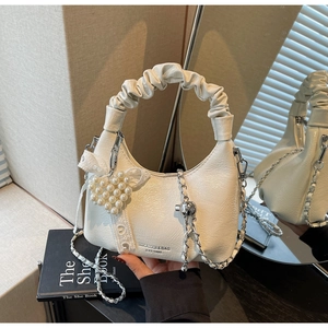 Detail der weißen Plissee-Handtasche mit Perlenherz-Anhänger und Spitzen-Schleife