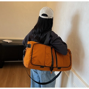 Orange canvas travel duffel bag shown on model back in a modern interior setting