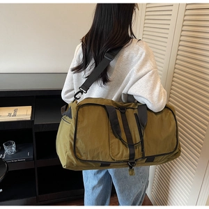 Olive green travel duffel bag with adjustable shoulder strap shown in a room setting
