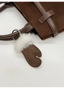 Nahaufnahme von Fausthandschuh-Anhänger aus braunem Wildlederimitat an Handtasche