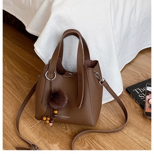 Détail d'un sac seau marron en cuir grainé avec pompon en fourrure et perles colorées