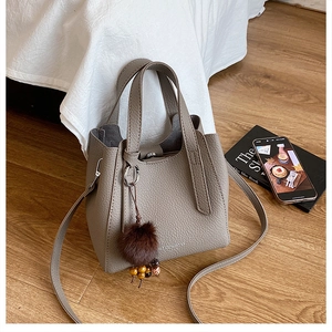 Détail du sac seau en cuir taupe avec pompon en fourrure et perles de bois décoratives