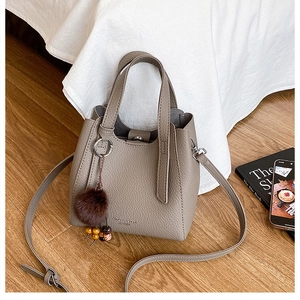 Détail du sac bandoulière taupe en cuir grainé avec pompon décoratif et perles en bois