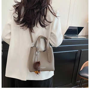 Gros plan d'un sac à main taupe grainé avec pompon en peluche et perles décoratives
