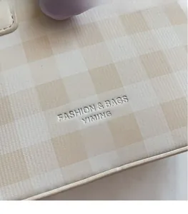 Vue détaillée du logo gravé argenté sur un sac seau beige à motif vichy texturé
