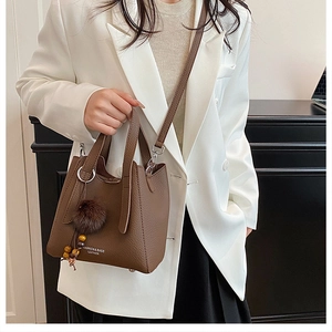 Sac bandoulière en cuir marron avec pompon porté par un mannequin en blazer blanc