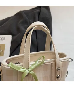 Vue détaillée du sac seau en cuir beige avec nœud en soie verte et rivets argentés
