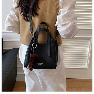 Détail du sac en cuir noir grainé avec lettrage mode et charmant pompon en peluche