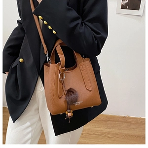 Détail du sac seau en cuir marron avec motif litchi, pompon en fourrure et bandoulière