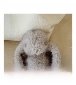 Close-up of fluffy grey bunny charm attached to a white pebbled leather handbag
