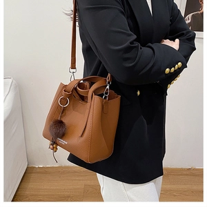 Sac seau en cuir marron porté par un mannequin avec pompon en peluche et perles