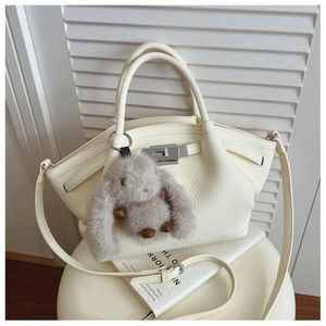 Close-up of beige lychee textured leather handbag with silver buckle and plush bunny charm
