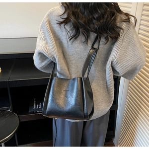 Detail einer schwarzen Leder-Eimertasche im Vintage-Stil, getragen zum grauen Pullover