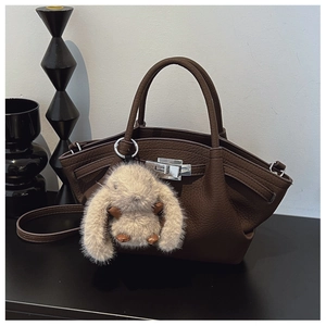 Detail of dark brown lychee leather handbag with metal clasp and plush rabbit charm