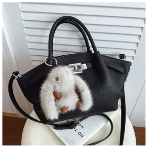 Close-up of black litchi grain leather handbag with a plush rabbit charm on a white stool
