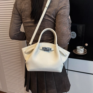 Close-up of white lychee leather handbag featuring silver twist lock and dual top handles