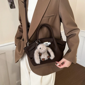 Close-up of dark brown lychee leather handbag with silver twist lock and plush bunny charm