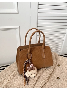 Gros plan d'un sac cabas en simili cuir marron avec un pendentif chien en peluche blanc