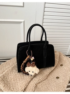 Détail d'un sac cabas noir avec une breloque chien en peluche et un nœud léopard