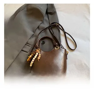 Detail of vintage brown leather bucket bag with gold logo and decorative beaded pendant