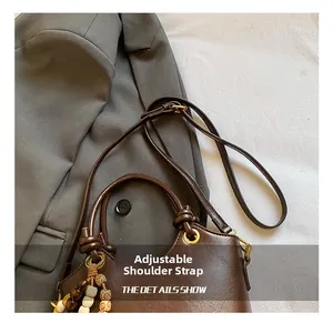 Close-up of brown leather bucket bag featuring a tassel with wooden beads and adjustable strap