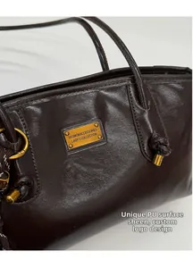 Detalle del bolso de hombro en cuero PU marrón oscuro con placa de metal y correa anudada